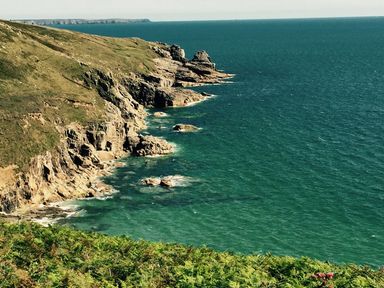 A rocky coastline with cliffs and green vegetation next to a blue sea at The Hayloft in Breage