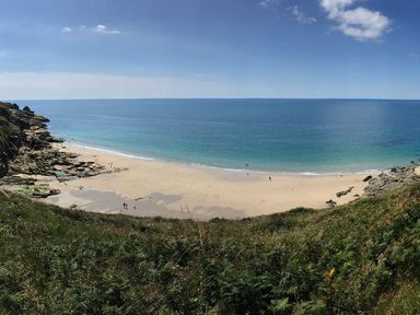 A beach with sand and rocks beside the ocean under a blue sky at The Hayloft in Breage