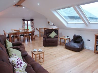 A living room with brown leather furniture wooden dining table and large skylight windows at The Hayloft in Breage