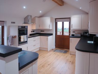 A kitchen with white cabinets black countertops wooden floor and a wooden door at The Hayloft in Breage