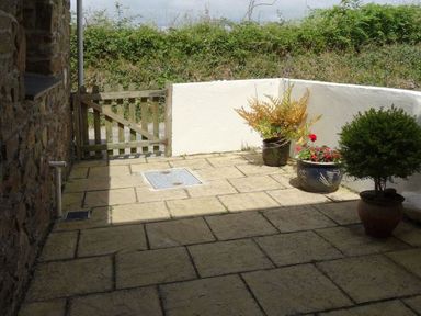 A paved outdoor patio area with three potted plants and a wooden gate at Badger Cottage in Mawgan-in-Meneage near Helston