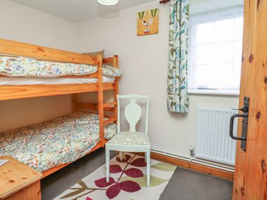 A small bedroom with bunk beds a chair and a window with patterned curtains at Badger Cottage in Mawgan-in-Meneage near Helston