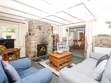 A living room with stone fireplace coffee table and chairs at Badger Cottage in Mawgan-in-Meneage near Helston