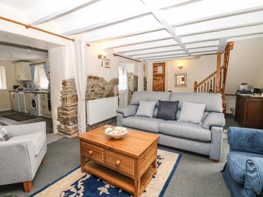 A living room with sofas a wooden coffee table and a doorway to a kitchen at Badger Cottage in Mawgan-in-Meneage near Helston