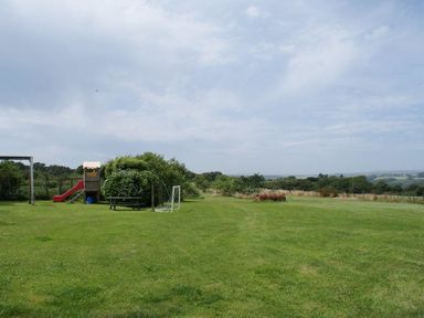 An outdoor grassy area with a swing set slide picnic table and small soccer goal with trees and countryside in the background at Swift Cottage in Mawgan-in-Meneage near Helston