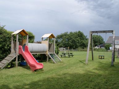 A playground with a red slide a wooden climbing frame a swing and a picnic bench in a grassy area at Swift Cottage in Mawgan-in-Meneage near Helston