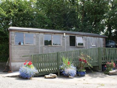 An exterior view of a wooden building with a ramp and flower pots in front at Swift Cottage in Mawgan-in-Meneage near Helston
