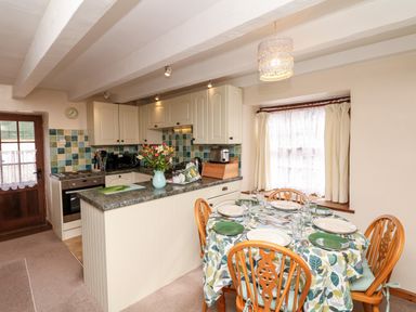 A kitchen and dining area with a dining table set for four and kitchen cabinets at Swift Cottage in Mawgan-in-Meneage near Helston