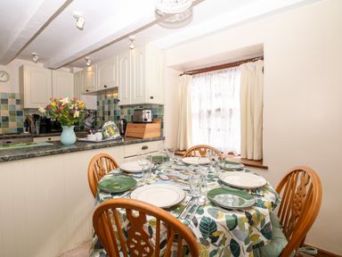 A dining area with a set table and a kitchen with cabinets and tiled backsplash at Swift Cottage in Mawgan-in-Meneage near Helston
