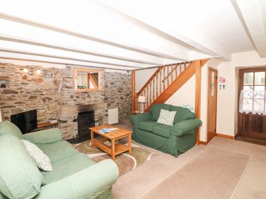 A living room with stone walls green sofas a wooden coffee table and a staircase at Swift Cottage in Mawgan-in-Meneage near Helston
