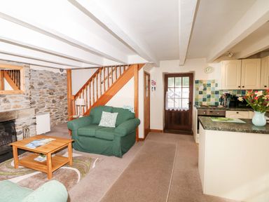 A living room with green armchairs wooden coffee table tiled kitchen and stone wall at Swift Cottage in Mawgan-in-Meneage near Helston