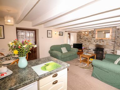 A living room with green sofas a stone fireplace a wooden coffee table and a vase of flowers on a countertop at Swift Cottage in Mawgan-in-Meneage near Helston