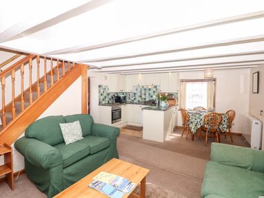 A living room with green sofas wooden stairs kitchen area with tiled backsplash and dining table at Swift Cottage in Mawgan-in-Meneage near Helston