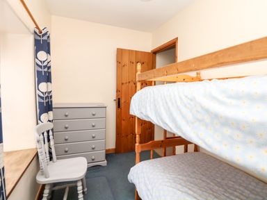 A small bedroom with bunk beds a gray chest of drawers and a gray chair at Swift Cottage in Mawgan-in-Meneage near Helston