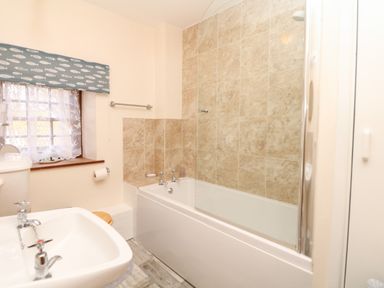 A bathroom with a bathtub and tiled walls a sink a window with patterned curtains and a toilet at Swift Cottage in Mawgan-in-Meneage near Helston