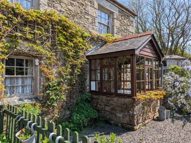A stone cottage with a wooden framed glass porch and climbing plants at Swift Cottage in Mawgan-in-Meneage near Helston