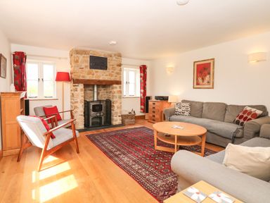 A living room with stone fireplace two armchairs, gray sofas, a wooden coffee table, red patterned rug and wooden floor at Marles Farmhouse in Salwayash