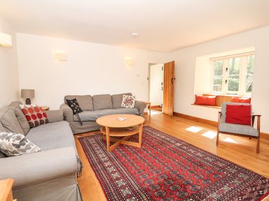 A living room with two grey sofas a wooden round coffee table a patterned red rug a window seat with cushions and a wooden chair at Marles Farmhouse Salwayash
