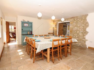 A dining room with a large table set with plates and glasses wooden chairs a green cabinet a floor lamp stone wall and three ceiling lights at Marles Farmhouse in Salwayash