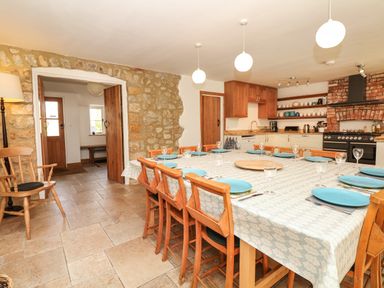 A dining area with a large table set with blue plates and glasses wooden chairs stone walls and a kitchen with wooden cabinets and a brick fireplace at Marles Farmhouse in Salwayash