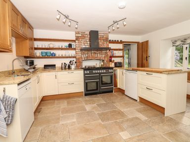 A kitchen with beige cabinets a brick chimney a black stove open shelves with dishes and a tiled floor at Marles Farmhouse in Salwayash
