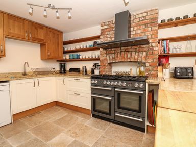 A kitchen with white cabinets wooden shelves and a black stove with a brick chimney at Marles Farmhouse in Salwayash