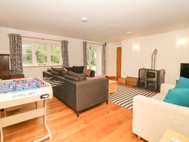 A living room with sofas a wood stove foosball table and windows with patterned curtains at Marles Farmhouse Salwayash