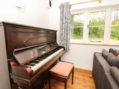 A room corner with an upright piano, piano bench, gray patterned curtains, window, and a gray sofa at Marles Farmhouse in Salwayash