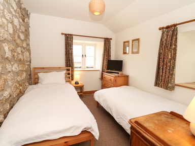 A bedroom with two single beds a stone wall a wooden dresser a small table with a lamp and a window with floral curtains at Marles Farmhouse in Salwayash