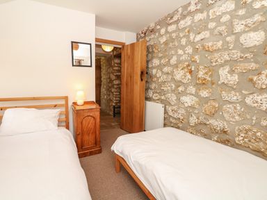 A bedroom with two single beds a wooden nightstand with a lamp a wooden door and a stone wall at Marles Farmhouse in Salwayash