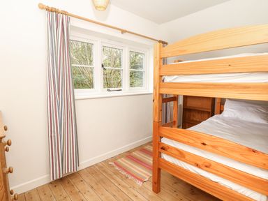 A bedroom with wooden bunk beds striped curtains under a window and a wooden chest of drawers at Marles Farmhouse in Salwayash