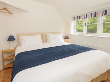 A bedroom with a large double bed white bedding blue runner two bedside tables with lamps and striped window blinds at Marles Farmhouse in Salwayash