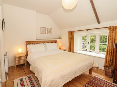 A bedroom with a double bed two bedside tables with lamps a window with curtains and wooden floorboards at Marles Farmhouse in Salwayash