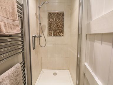 A tiled shower area with a handheld showerhead a mosaic tile niche and towels on a heated towel rail at Marles Farmhouse in Salwayash
