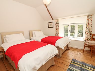 A bedroom with two single beds and red blankets near a window with patterned curtains at Marles Farmhouse in Salwayash