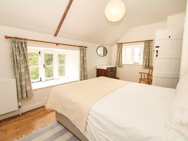 A bedroom with a bed a wooden chest of drawers a wooden chair striped rug and two windows at Marles Farmhouse in Salwayash