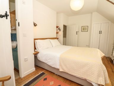 A bedroom with a double bed a yellow bedspread wooden floors a small rug and a door to a bathroom at Marles Farmhouse in Salwayash