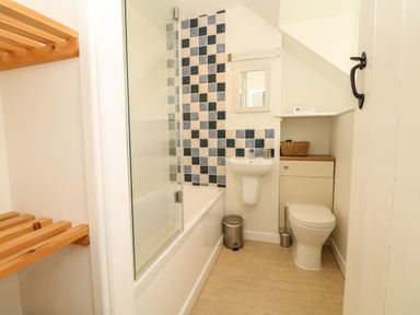 A bathroom with a bathtub and shower with blue and white tiles a white sink a white toilet and wooden shelves at Marles Farmhouse in Salwayash