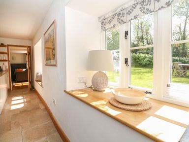 A hallway with a lamp and a bowl on a wooden windowsill overlooking a garden at Marles Farmhouse in Salwayash
