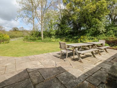A garden patio with two wooden picnic tables and chairs surrounded by grass trees and bushes at Marles Farmhouse in Salwayash