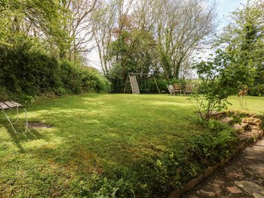 A garden with a swing set and wooden table and chairs surrounded by trees and shrubs at Marles Farmhouse in Salwayash