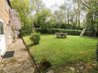 A garden with a stone path beside a house lawn table and chairs and a children's swing set at Marles Farmhouse in Salwayash
