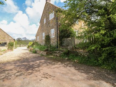 A gravel driveway beside a stone house with white windows and a wooden gate surrounded by greenery at Marles Farmhouse in Salwayash
