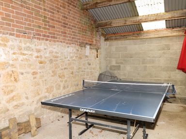 A ping pong table in a room with brick and stone walls and a corrugated roof at Marles Farmhouse in Salwayash
