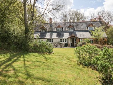 A stone and white cottage with a slate roof and dormer windows surrounded by trees and grass at Marles Farmhouse in Salwayash