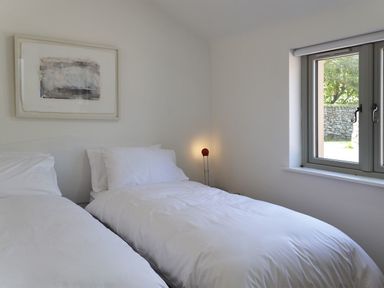 A bedroom with two single beds white bedding a window and a framed abstract painting at The Studio in Rinsey Cove near Praa Sands