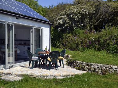 An outdoor patio with a table and four chairs outside a house with solar panels at The Studio in Rinsey Cove near Praa Sands