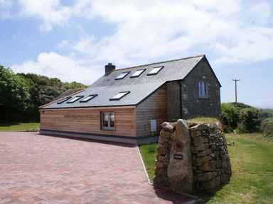 A stone and wood house with skylights on a paved driveway and a stone marker at The Studio in Rinsey Cove near Praa Sands