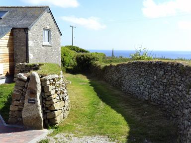 A stone house with a pathway and stone walls leading to the sea at The Studio in Rinsey Cove near Praa Sands