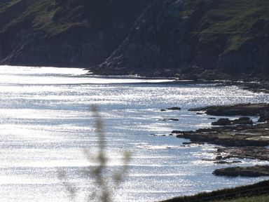 A coastal scene with rocky cliffs and sunlight reflecting off the water at The Studio Rinsey Cove near Praa Sands